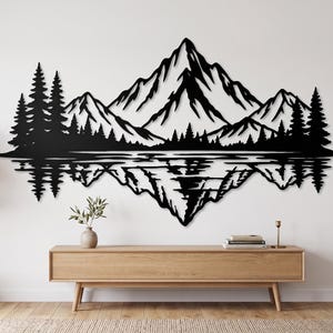 May include: A black metal wall art piece featuring a detailed silhouette of a mountain range with pine trees and a mirrored reflection effect. The design depicts jagged peaks and a dense forest line, creating a symmetrical landscape scene.