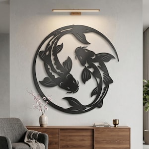 Peut inclure: Décoration murale en métal noir représentant des carpes koï. L'œuvre d'art montre deux poissons nageant en cercle. L'art mural est fixé sur un mur clair au-dessus d'un meuble en bois. Un fauteuil gris et une plante sont dans la pièce.