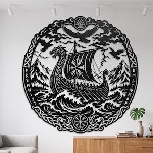 Op de afbeelding: Een cirkelvormig wandkunstwerk van zwart metaal met een gedetailleerd Vikingschip op gestileerde golven. Het ontwerp bevat een boeg in de vorm van een draak, een zeil met een Vegvisir-symbool, vliegende raven, bergen en een rand met runen.