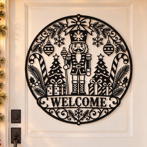 May include: A circular black metal wall sign featuring a laser-cut design of a nutcracker, Christmas trees, wrapped gifts, candy canes, and hanging ornaments. The word WELCOME is centered at the bottom of the circular frame with snowflake accents.