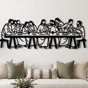 Puede incluir: Arte mural de metal negro que representa la Última Cena. La obra presenta una larga mesa con figuras sentadas alrededor, todo en un estilo minimalista de línea. Está montada en una pared blanca sobre un sofá.