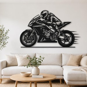 Peut inclure: Décoration murale en métal noir représentant une moto et son pilote en combinaison de course. La moto est en mouvement, avec des lignes de vitesse. L'œuvre est fixée sur un mur blanc, idéale pour un salon.