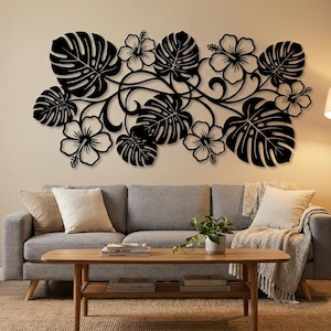 Pode incluir: Arte de parede em metal preto com um design tropical de folhas de monstera e flores de hibisco. A obra de arte é montada acima de um sofá cinzento, adicionando um toque de decoração inspirada na natureza à sala de estar. Design moderno e elegante.
