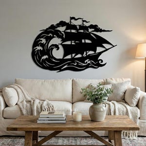 Peut inclure: Une œuvre d'art murale en métal noir représentant un voilier sur une mer orageuse. L'œuvre présente un navire avec des voiles gonflées, sur fond de vagues déferlantes et de nuages sombres. Elle est installée au-dessus d'un canapé crème.