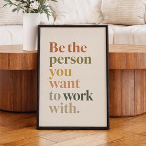 以下が含まれることがあります： 「Be the person you want to work with.」というテキストが書かれた長方形の額入りウォールアートプリント。文字はテラコッタ、オリーブグリーン、マスタードイエロー、セージグリーンなどの様々な色で、クリーム色の背景に積み重ねるように配置されています。