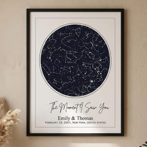 Puede incluir: Impresión enmarcada con un mapa celeste azul oscuro dentro de un borde blanco. El texto "The Moment I Saw You" está sobre los nombres "Emily & Thomas" y la fecha y lugar: 23 de febrero de 2001, Nueva York, Estados Unidos.