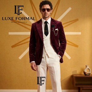 May include: A burgundy velvet suit with a white vest and flared white pants. The suit includes a black tie and a pocket square. The image also displays the text "LUXE FORMAL RETRO APPARELS".
