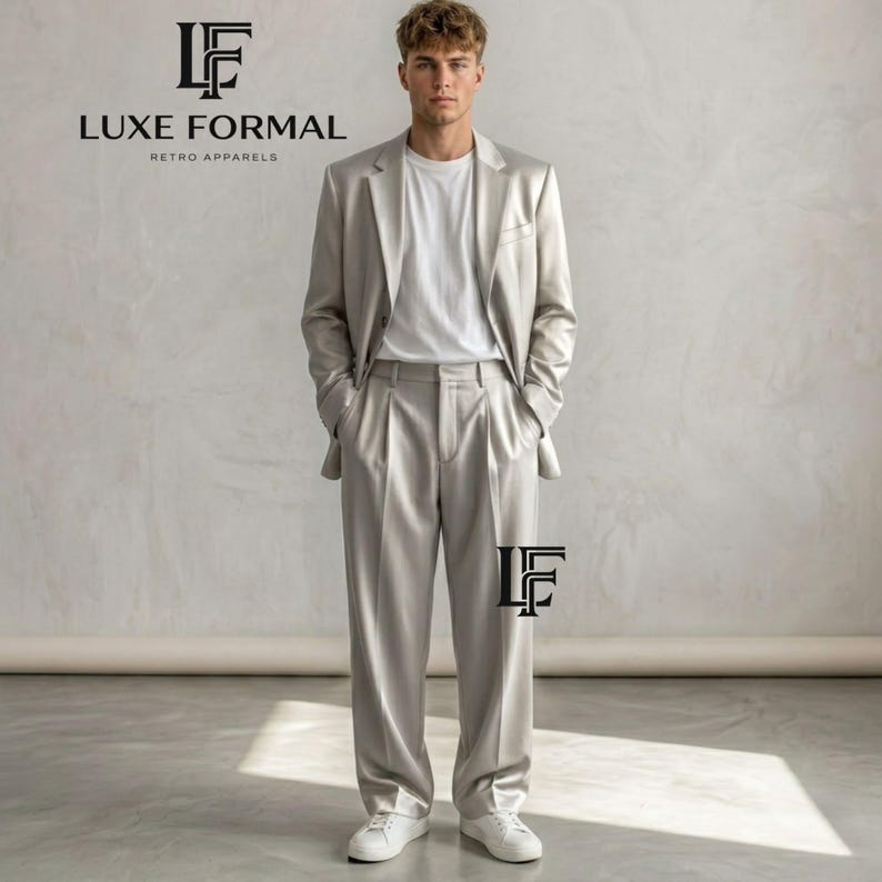 Puede incluir: Un traje gris claro con una chaqueta y pantalones plisados a juego, combinado con una camiseta blanca y zapatillas blancas. El texto "LUXE FORMAL RETRO APPARELS" se muestra en negro. El traje es una versi&oacute;n moderna de la moda retro.