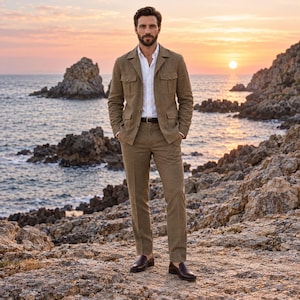 May include: A tan safari-style jacket with four front pockets and matching trousers, worn over a crisp white button-down shirt with a dark brown leather belt and dark brown leather loafers, creating a coordinated ensemble for a formal look.