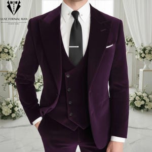Puede incluir: Un traje de tres piezas de terciopelo morado oscuro que incluye una chaqueta de botonadura sencilla con solapas de pico, un chaleco a juego, una camisa blanca de cuello rígido y una corbata negra lisa con un pasador plateado.