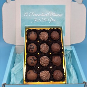May include: A light blue gift box containing twelve chocolate truffles in a gold-edged tray. The truffles are various shades of brown and have different toppings. The box lid has the text "A Personalised Message Just For You".