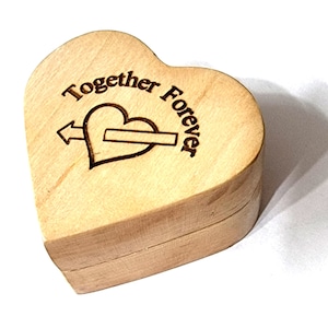 Può includere: Una scatola di legno a forma di cuore con un coperchio. La scatola è incisa con le parole "Together Forever" e un cuore con una freccia che lo attraversa.