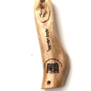 Puede incluir: Una caja de mezuzá de madera con texto hebreo y una estrella de David tallada. El texto dice "Shema Yisrael Adonai Eloheinu Adonai Echad" que se traduce como "Escucha, Israel, el Señor nuestro Dios, el Señor es Uno".