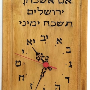 May include: A wooden clock with a red minute hand and black hour hand. The clock face is engraved with Hebrew text, including the words "If I forget you, Jerusalem".