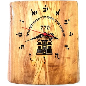 Puede incluir: Un reloj de madera con una aguja de segundos roja y una imagen en blanco y negro de un edificio. La esfera del reloj tiene texto en hebreo y el número 770.