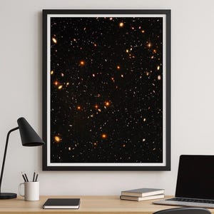 Può includere: Stampa incorniciata di un'immagine dello spazio profondo, che mostra una vasta distesa di stelle e galassie su uno sfondo nero. I corpi celesti sono raffigurati in varie dimensioni e tonalità di arancione e bianco, creando un'esposizione cosmica.