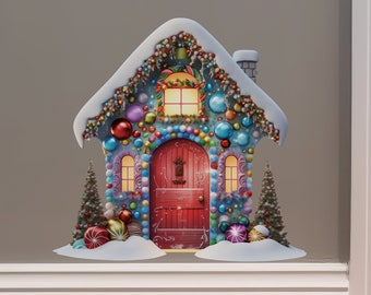 Puede incluir: Una casa de jengibre decorada con caramelos coloridos, adornos y una puerta roja. La casa está cubierta de nieve y tiene un techo nevado.