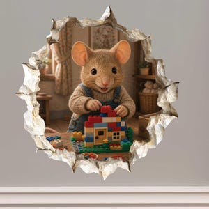 May include: A wall decal featuring a trompe l'oeil effect of a hole in the wall revealing a brown mouse wearing a beige sweater and blue overalls. The mouse is building a small house with colorful plastic construction bricks on a wooden table.
