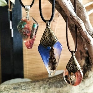 Peut inclure: Trois colliers pendentifs uniques avec des cordons noirs. Les pendentifs en forme de diamant et de goutte d'eau présentent de la résine avec des éléments naturels incrustés et des accents métalliques couleur bronze antique. Les couleurs incluent le rouge, le bleu et le transparent.