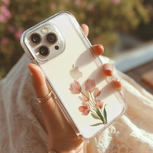 Könnte beinhalten: Transparente Handyhülle mit einem Blumendesign aus rosa Tulpen und grünen Blättern. Die Hülle hat einen transparenten Rand. Das Telefon hat eine silberne Kamera und das Apple-Logo.