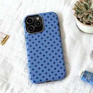 May include: A blue phone case with a pattern of dark blue polka dots. The case has a glossy finish and a camera cutout. The phone case is on a white surface.