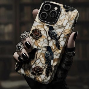 May include: A smartphone case featuring a stained glass design with black crows, dark roses, and golden leaves on a white background. The case has a black camera module cutout and a glossy finish, showcasing a detailed mosaic pattern of birds and floral elements.