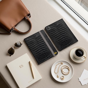 May include: A brown leather handbag, black crocodile-textured tablet case, black crocodile-textured notebook with a grey elastic band and gold BD initials, sunglasses, white journal with ES initials, gold pen, gold jewellery, and a coffee cup.
