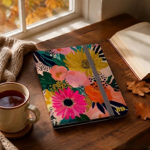 May include: A rectangular notebook featuring a vibrant floral pattern with large pink, yellow, and orange flowers against a dark green and pink background. A grey elastic band secures the cover, which displays the gold-coloured initials BD.