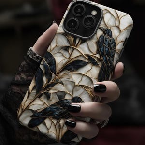 May include: A smartphone case featuring a stained-glass style design with cream-coloured segments outlined in gold. The pattern depicts dark blue and black birds perched among leafy branches, creating a mosaic effect across the entire back surface.