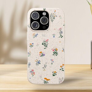 May include: A phone case with a floral pattern. The case is off-white with a speckled texture and features a repeating pattern of colorful flowers in shades of pink, orange, blue, and purple. The case has a camera cutout.