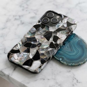 May include: A smartphone case featuring a mosaic pattern of iridescent mother-of-pearl shell fragments and solid black geometric pieces. The case has a cutout for a triple-lens camera system and is positioned next to a blue agate slice.