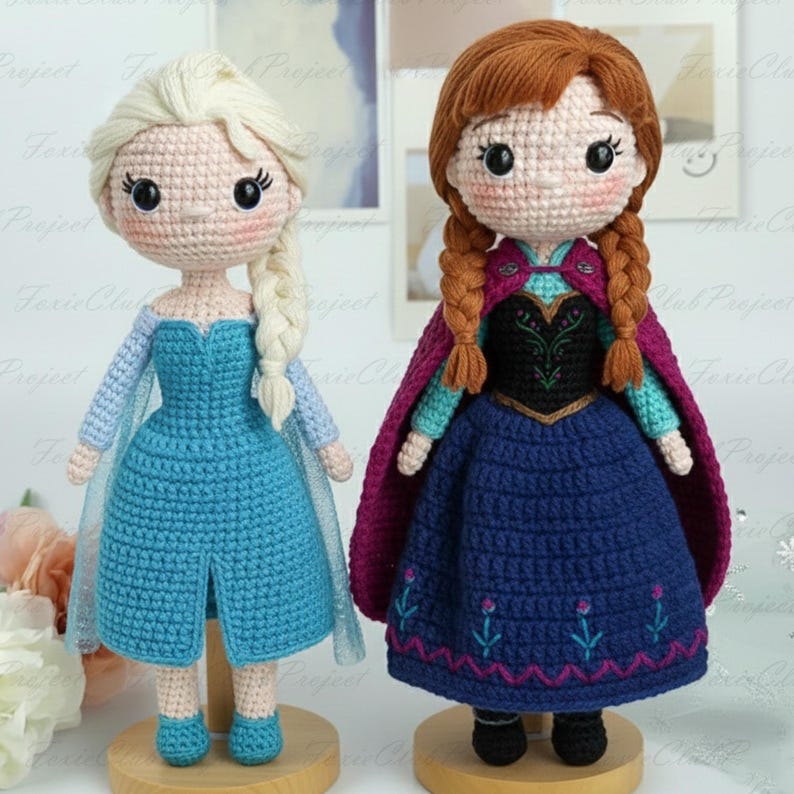 May include: Two handmade crochet dolls, one with blonde hair in a braid and a blue dress, the other with auburn braids and a blue dress with a purple cape. Both dolls are on wooden stands and have detailed facial features.