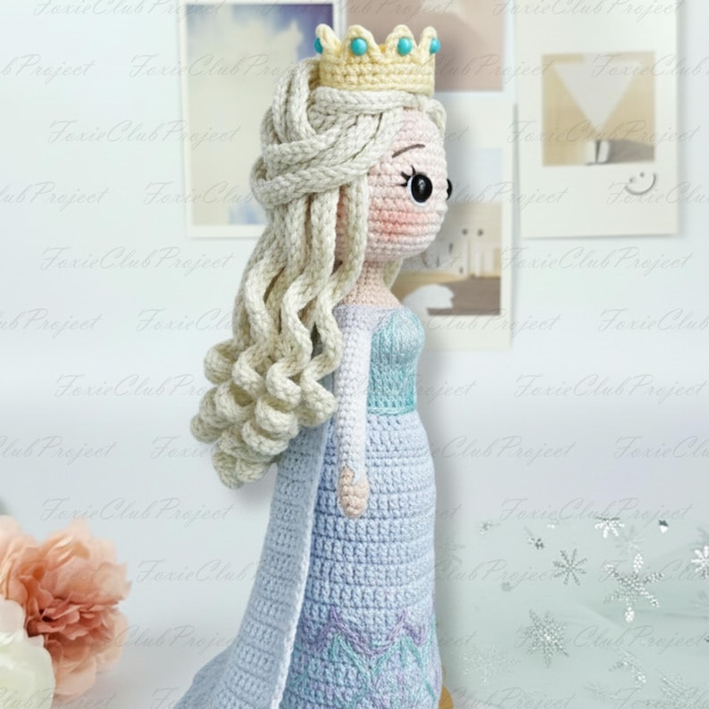 May include: A handmade crochet doll of a princess, featuring a light blue dress with a long cape, blonde hair, and a golden crown with turquoise accents. The doll is approximately 30 cm tall, suitable for children's play or room decor.