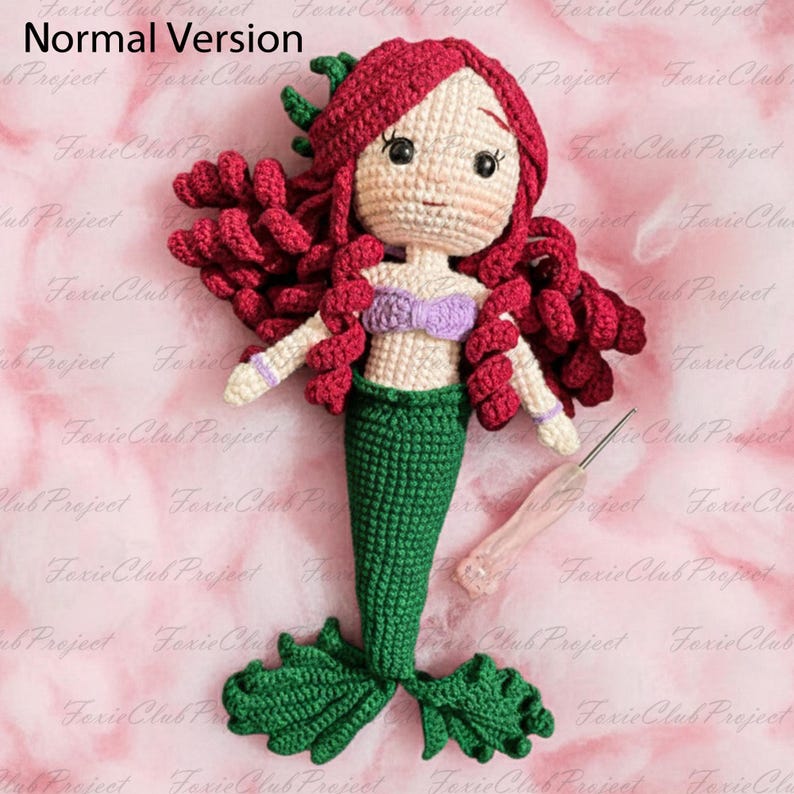 May include: A handmade crochet mermaid doll with red hair, a purple top, and a green tail. The doll has a cream-colored face and arms, with black eyes. The mermaid is holding a crochet hook.