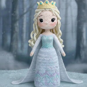 May include: Crocheted doll of a princess wearing a light blue dress with a long cape. The doll has blonde hair, a yellow crown, and a light pink face. The dress has a detailed pattern at the bottom. The doll is approximately 30 cm tall.