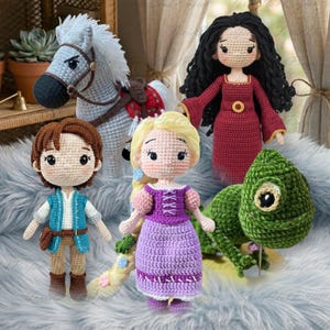 Könnte beinhalten: Eine Sammlung handgefertigter Häkelpuppen und -figuren, darunter ein weißes Pferd, eine Puppe in einem roten Kleid, eine Puppe in einem lila Kleid, eine Puppe in einem blauen Outfit und ein grünes Chamäleon. Die Puppen haben detaillierte Merkmale und sind auf einer flauschigen Oberfläche ausgestellt.