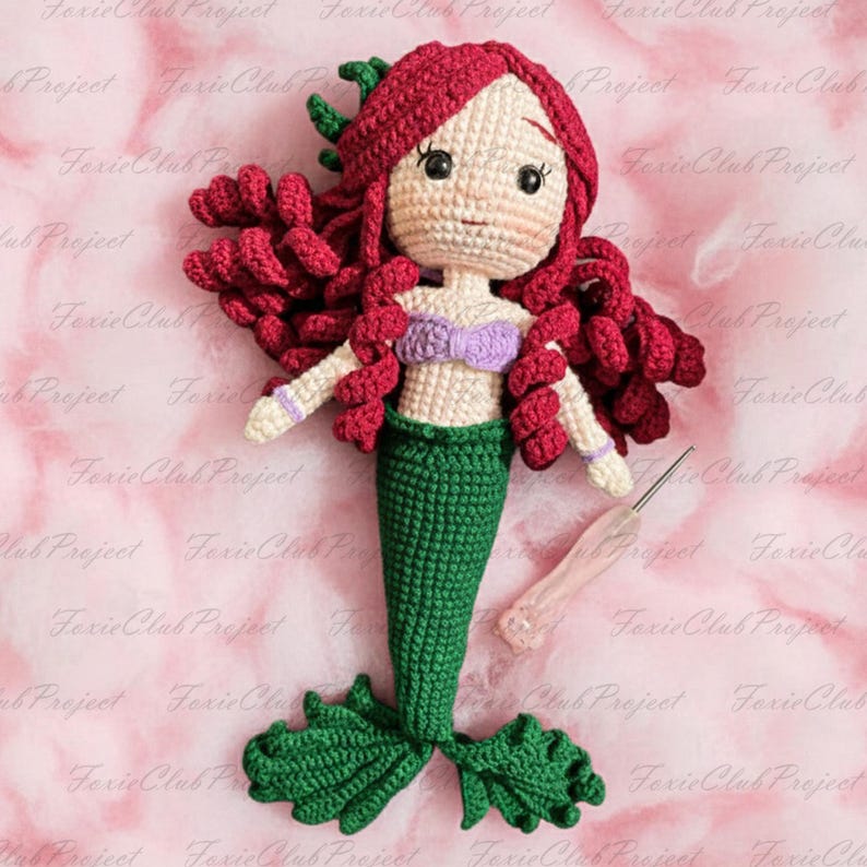 May include: A handmade crochet mermaid doll with red hair, a purple top, and a green tail. The doll has a cream-colored face and is holding a crochet hook. The doll is a whimsical, handcrafted item.