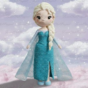May include: A handmade crochet doll of a character with blonde hair in a side braid. The doll wears a turquoise dress with a slit and a sheer cape. The doll's face has embroidered features and is wearing blue shoes. The doll is approximately 10 inches tall.