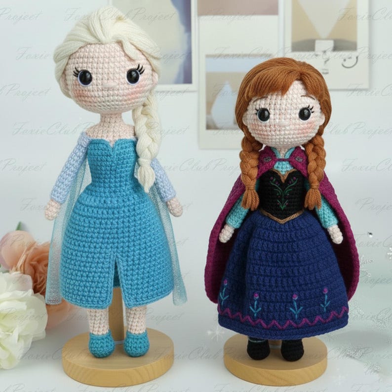 May include: Two handmade crochet dolls. One has blonde hair in a side braid and wears a blue dress, the other has auburn hair in braids and wears a blue dress and a purple cape. Both dolls are on wooden stands.