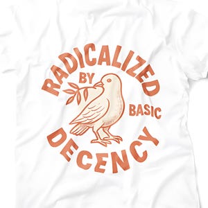 May include: White t-shirt with a rust-coloured design. The design features a dove with an olive branch, surrounded by the words "RADICALIZED BY BASIC DECENCY". The text and image are centered.