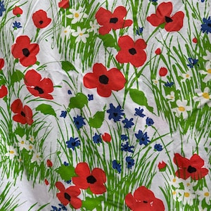 May include: White fabric with a vibrant floral pattern featuring red poppies, blue wildflowers, and white daisies amidst green grass and leaves. The design is repeated across the fabric.