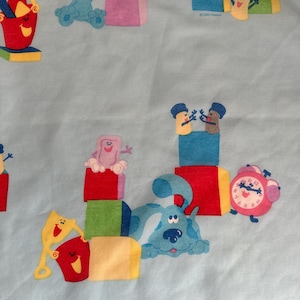 May include: A light blue fabric featuring a repeating pattern of Blue's Clues characters including Blue the dog, Tickety Tock the clock, and various colorful building blocks, buckets, and shovels in shades of red, yellow, green, and pink.