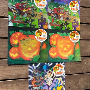 Puede incluir: Una colección de decoraciones 3-Décor con temática de Halloween. Las decoraciones presentan ilustraciones de dibujos animados de calabazas, un coche espeluznante y un monstruo. Cada decoración tiene una pegatina "try me!"
