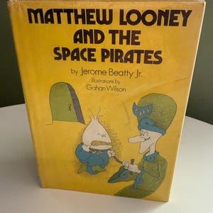 May include: A hardcover book titled Matthew Looney and the Space Pirates by Jerome Beatty Jr. with illustrations by Gahan Wilson. The yellow cover features a cartoon drawing of two characters, one in blue and one in green, near a green door.