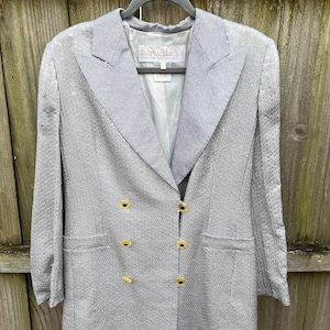 May include: A silver blazer with a double breasted closure and gold buttons. The blazer has a label that reads "EScada Munich, Germany".