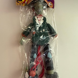 May include: A wooden marionette puppet in a green jacket and black trousers, packaged in a clear plastic bag with a Halloween-themed header card featuring a pumpkin illustration and the text Halloween.