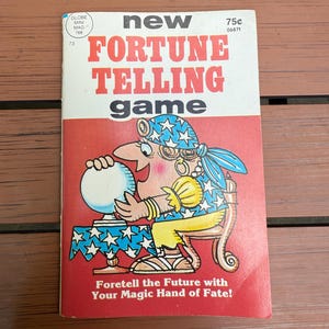 May include: A vintage "New Fortune Telling Game" book cover. The cover features a cartoon fortune teller with a crystal ball, set against a red background. Text includes "Foretell the Future with Your Magic Hand of Fate!"