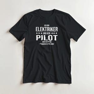 Pode incluir: Camiseta preta com texto branco. O texto diz "ICH BIN ELEKTRIKER UND KEIN PILOT" acima de "ABER ICH BRING SPANNUNG IN JEDE HÖHE". A camisa é de estilo gola redonda.