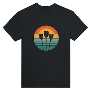 May include: Black t-shirt with a retro design of three darts set against a sunset backdrop. The graphic includes a circle with orange, yellow, and teal horizontal stripes. The darts are black with red and yellow accents.