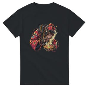 以下が含まれることがあります： 黒いTシャツ。赤と黒の衣装を着た猿がラーメンを食べている詳細なイラスト。アートワークは、食べ物から蒸気が立ち上る、鮮やかな漫画のスタイルです。猿は帽子とヘッドホンを着用しています。